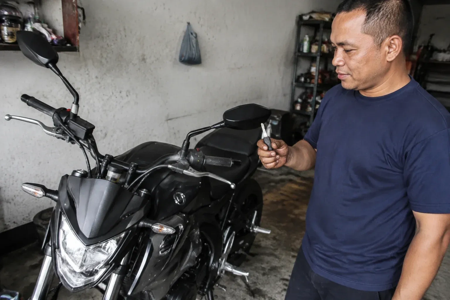 Person holding a key beside a black motorcycle in a garage. — Motorcycle & Scooter Keys, Whitby