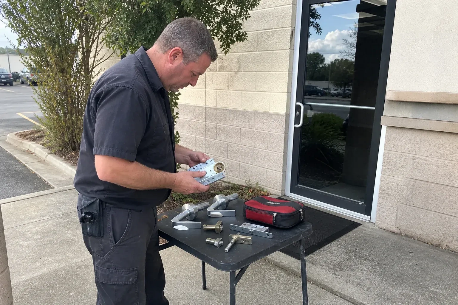 Technician examining detached commercial lock hardware on a table outside a shop entrance. — Business Lockout Service, Whitby